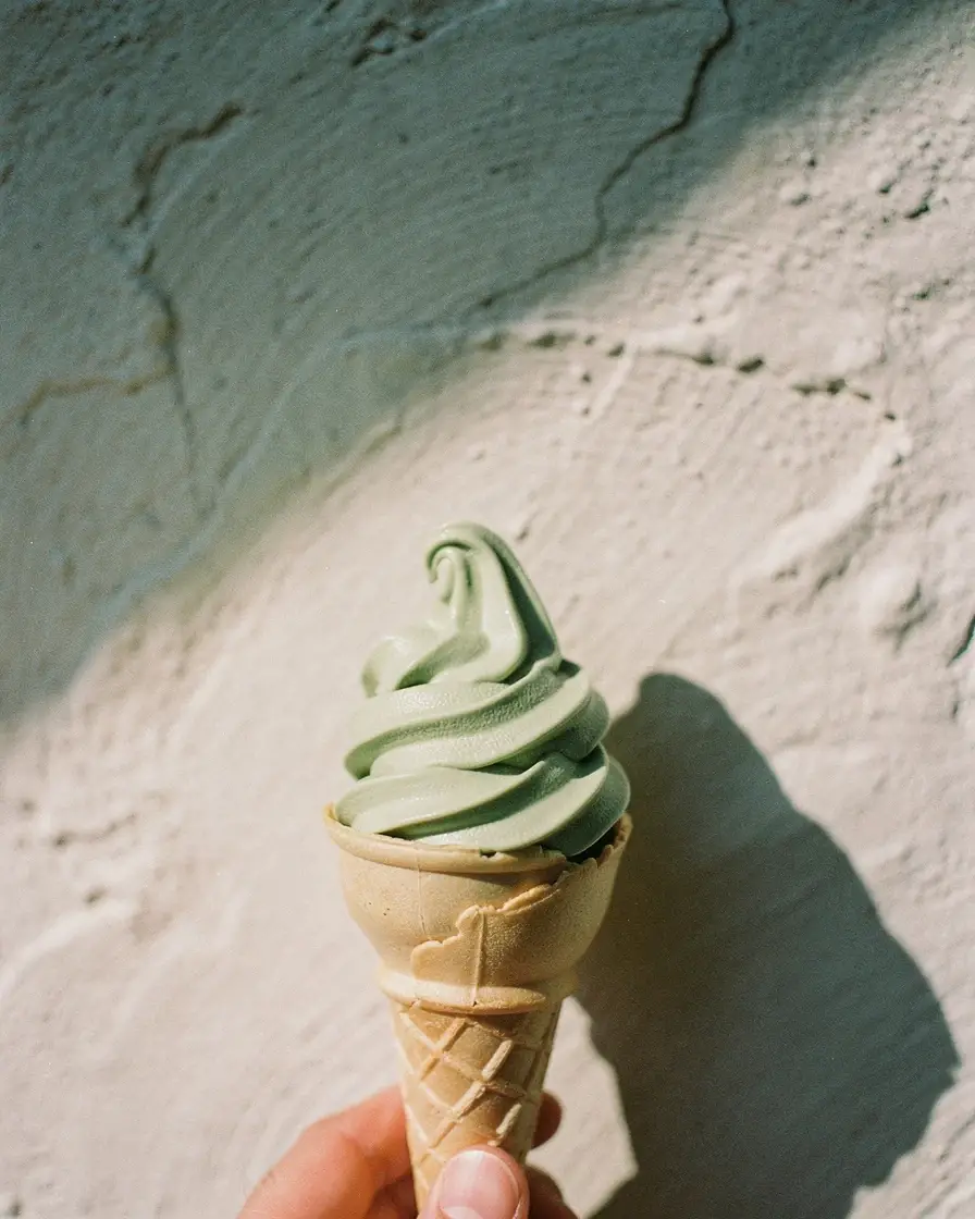 Matcha soft-serve in a cone against a sunlit plaster wall