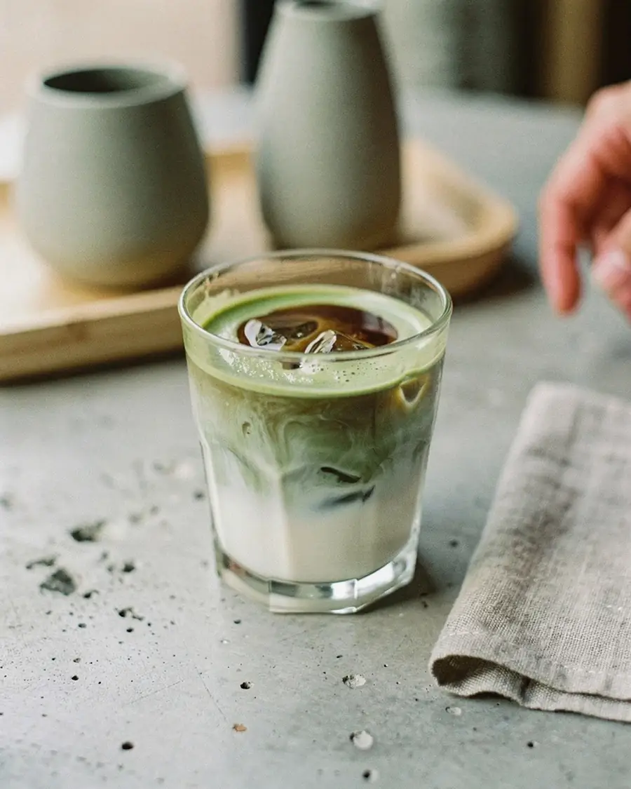 Espresso poured over iced matcha and milk in a short glass