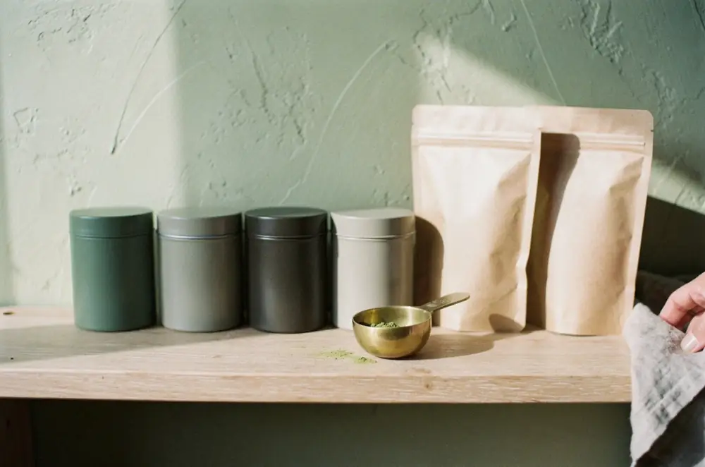 Unlabelled tea tins and pouches on an oak shelf